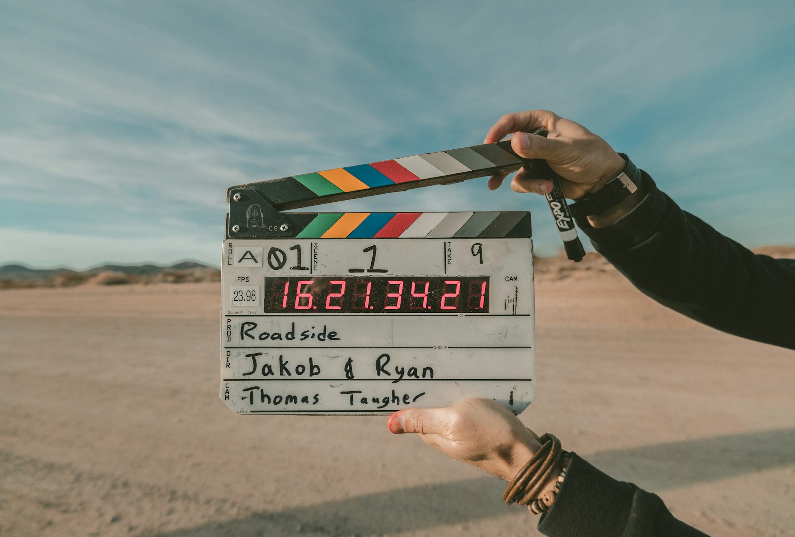 Film clapperboard on a desert road at sunset, cinematographer in background