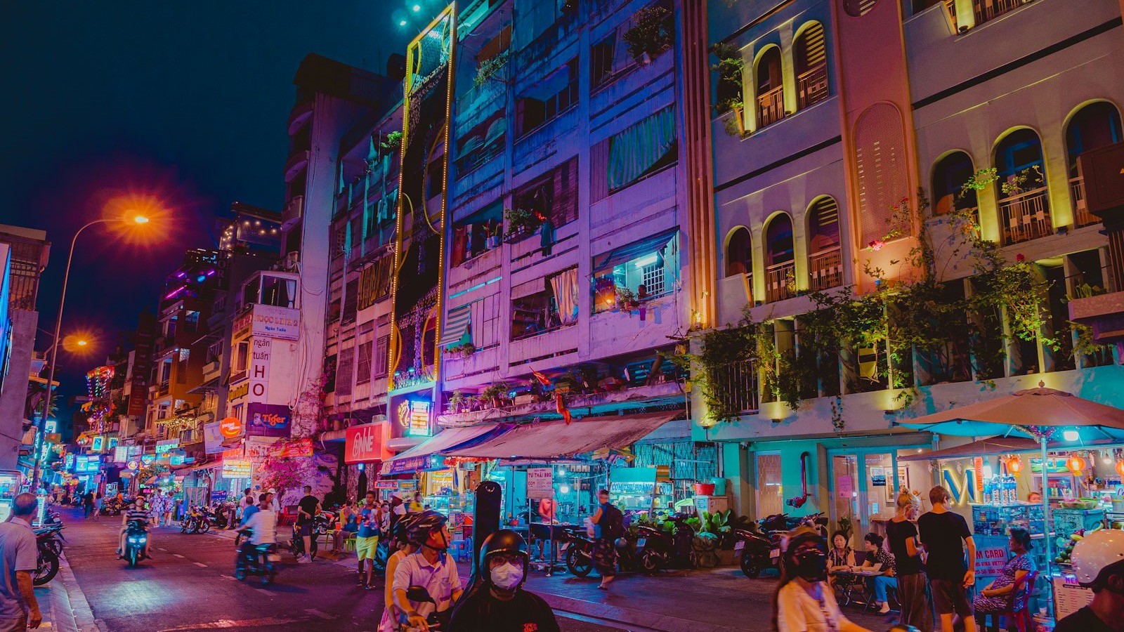 Neon lit street in Ho Chi Minh City at night with pedestrians and motorbikes