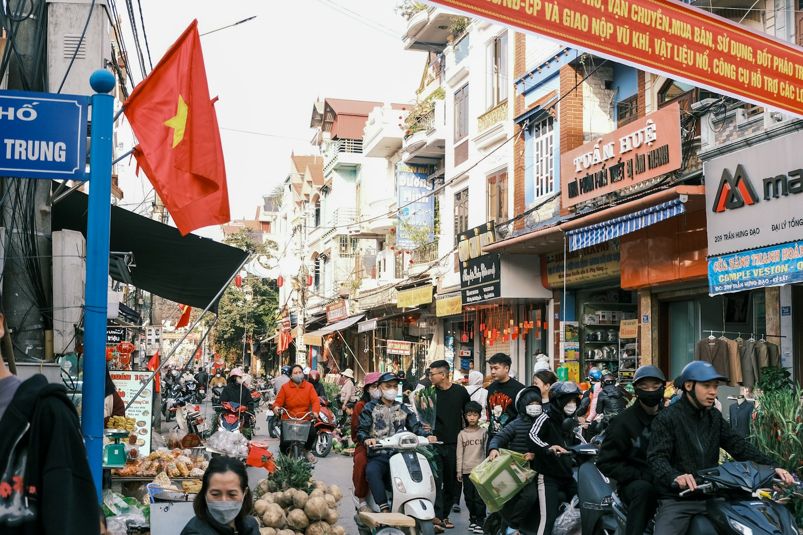 A busy Vietnamese street market with flags, scooters and shop fronts