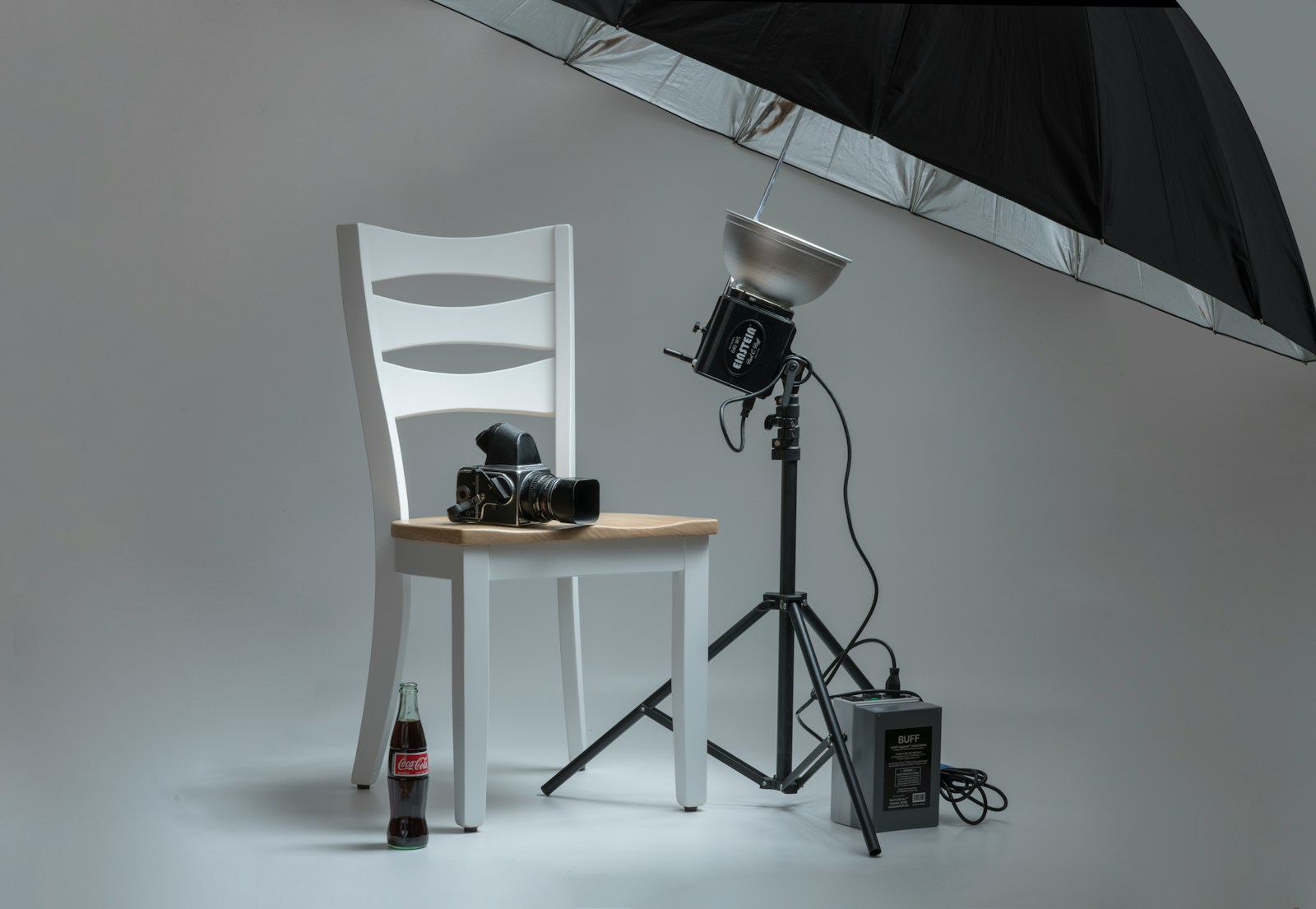 A product photography set with a camera, strobe and umbrella arranged around a glass bottle in a studio